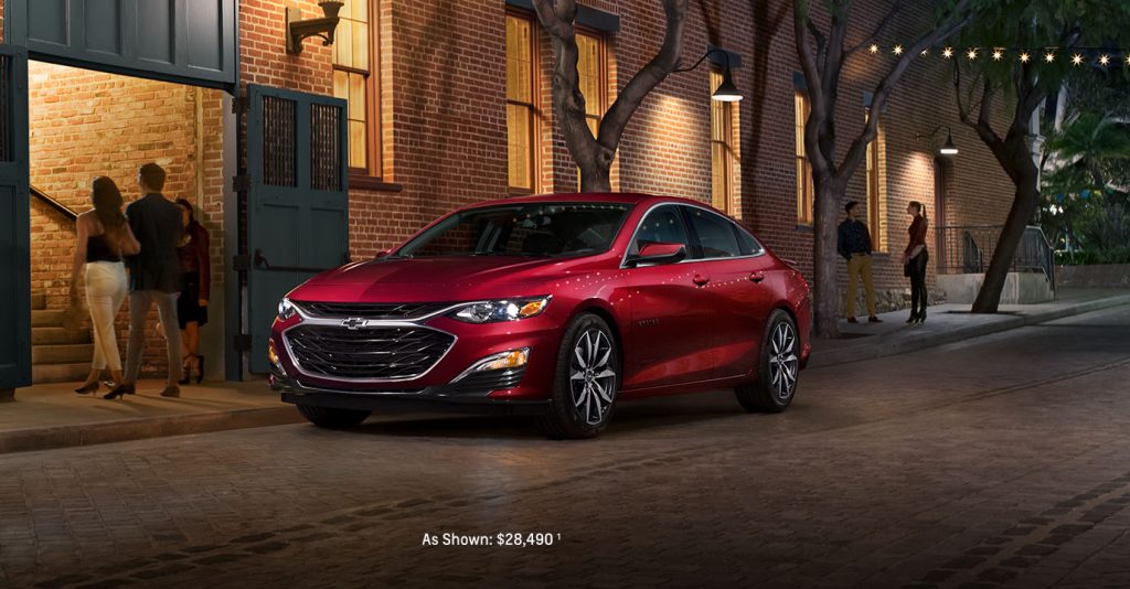 A red 2025 Chevy Malibu parked along a brick building in downtown Amsterdam, New York