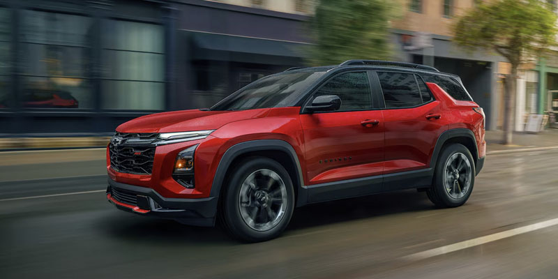 A Red 2025 Chevrolet Equinox driving through a city street in downtown Amsterdam, New York.