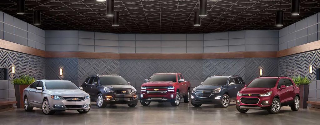 Lineup of 2025 Chevrolet SUVs and trucks displayed in a modern showroom in Amsterdam, featuring various Chevy models in different colors and body styles.