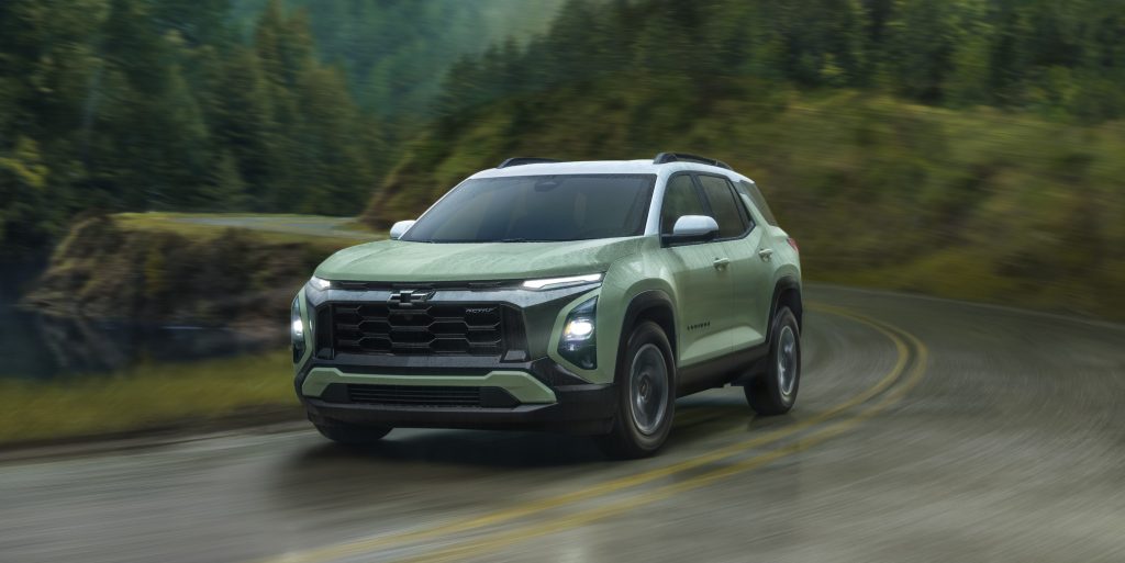 A green 2025 Chevrolet Equinox drives along a winding road in a wooded area.