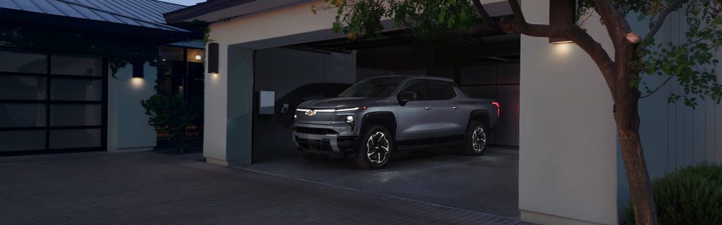2025 Chevrolet Silverado EV parked in a modern home garage, charging with an electric station, showcasing advanced electric truck design.
