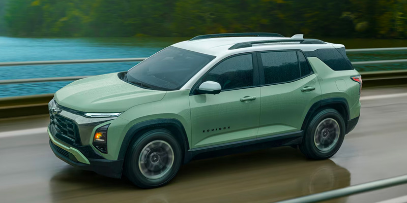 Side view of a light green Chevrolet Equinox SUV driving on a highway, with motion blur and a scenic water and guardrail background.