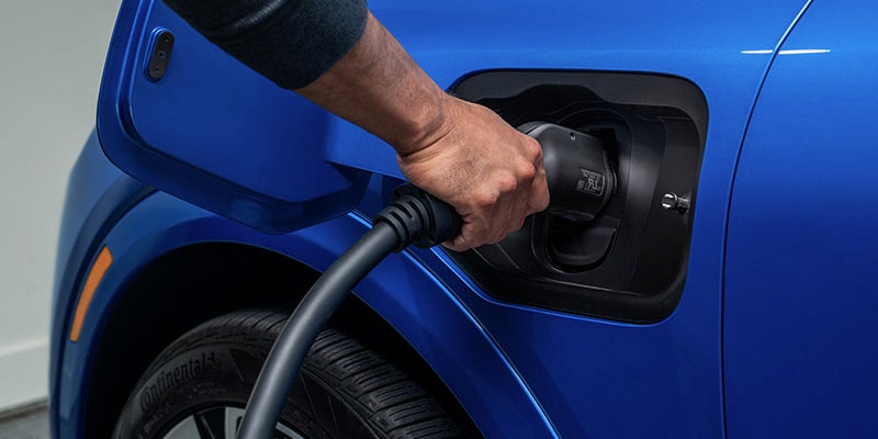 Close-up of a man’s hand plugging in a charging cable to a blue 2025 Chevrolet Equinox EV.