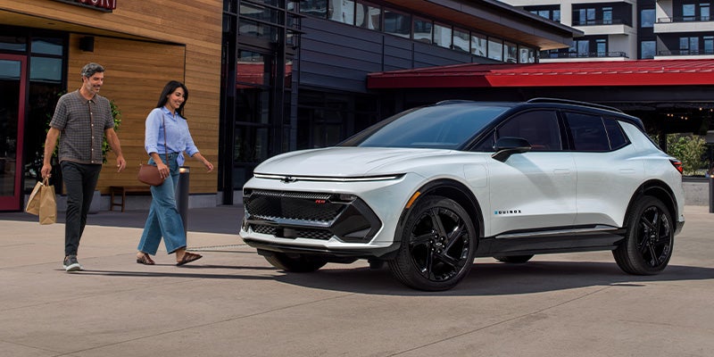 A couple walks toward a white 2025 Chevrolet Equinox EV parked outside a restaurant