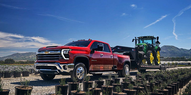 Red Chevrolet Silverado HD towing a trailer carrying a green tractor.