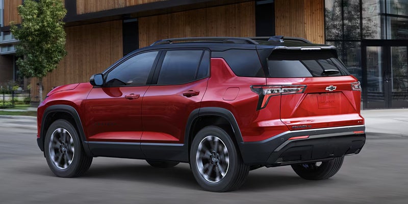 Red Chevrolet Traverse driving past a modern building.