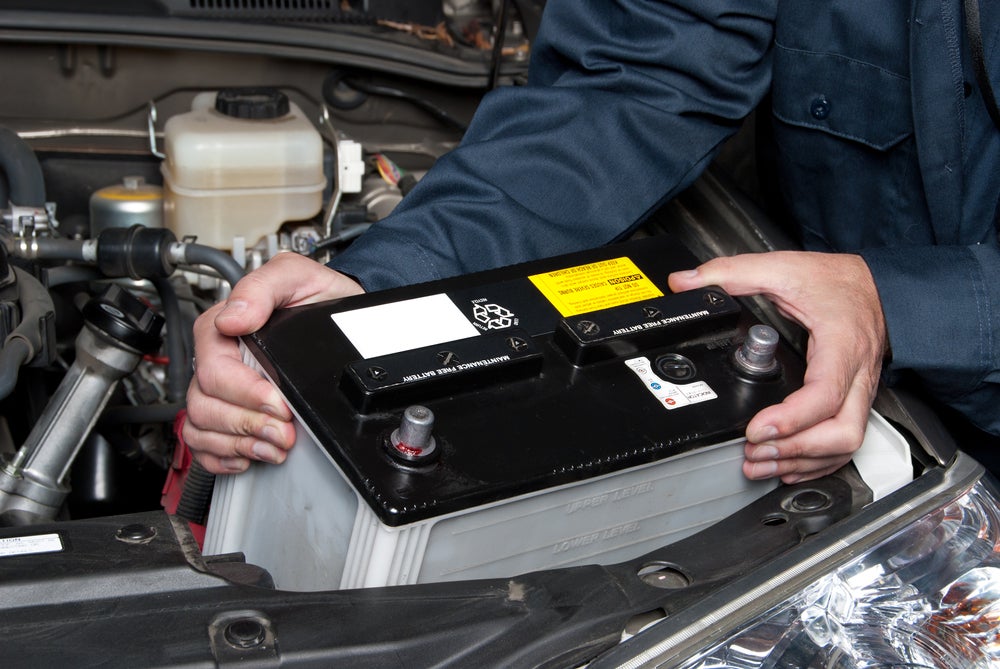 Technician replacing a car battery under the vehicle hood.